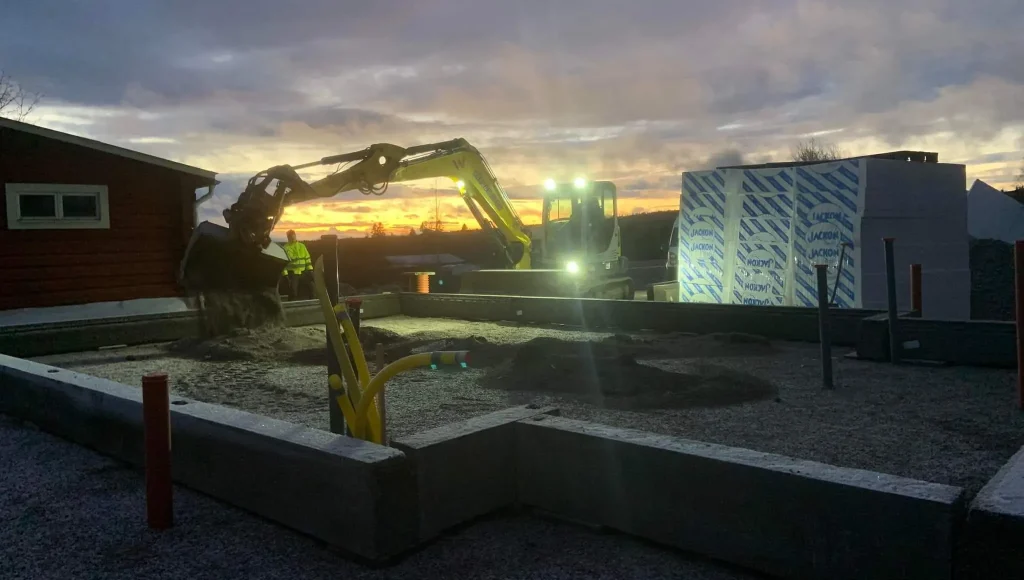 Grävmaskin vid grundarbete i kvällsljus