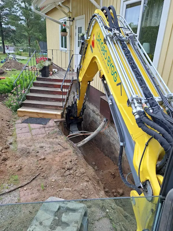 Grävmaskin gräver vid husets trappa